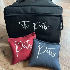 May include: A black canvas bag with a zipper closure and the text "The Petts" printed in white. Two bean bags are included, one red with the text "The Petts" in white and one blue with the text "The Petts" in white.