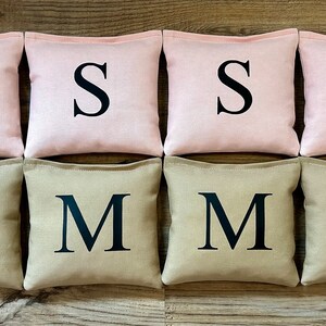 May include: Eight bean bags, four pink and four beige, with the letter 'S' on the pink bags and the letter 'M' on the beige bags.