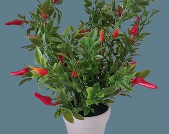 May include: A potted artificial plant with green leaves and red chili peppers. The plant is in a white ceramic pot.