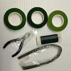 May include: An overhead shot of floral arranging supplies. Three rolls of green floral tape, a pair of black and silver wire cutters, a spool of dark green floral wire, and a green floral stem wrap are visible.