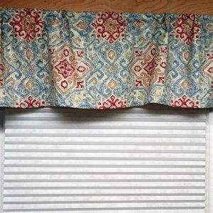 May include: A blue, red, and beige patterned valance with a white window blind behind it.