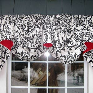 May include: A window valance with a black and white damask pattern and red accents. The fabric is gathered and draped over a window, adding a decorative touch to the room. The valance is mounted on a dark rod.
