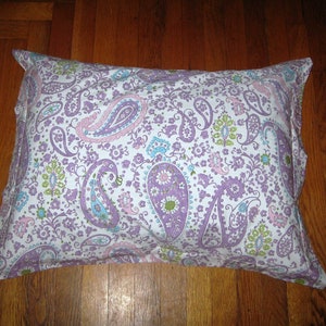 May include: A white pillowcase with a paisley pattern in shades of purple, pink, and green. The pillowcase has a white background with a floral design.