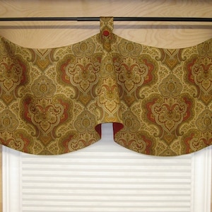 May include: A valance with a paisley pattern in shades of gold, brown, and red. The valance has a curved shape and is hung on a black rod.