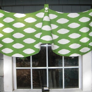 May include: A green and white patterned valance with a scalloped edge hangs over a window. The valance is made of a fabric with a white leaf design on a green background.