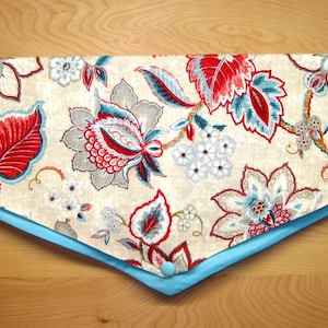 May include: A valance with a floral pattern in shades of red, blue, and gray. The valance is lined with a light blue fabric and has a scalloped edge.