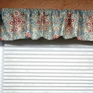 May include: A blue and beige patterned valance with red accents hangs above a white window blind.