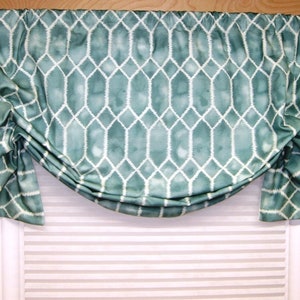 May include: A teal valance with a white geometric pattern resembling a chicken wire fence. The valance is gathered and draped over a white window blind.