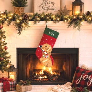 May include: A red Christmas stocking featuring a golden dog holding a candy cane in its mouth. The stocking has a green cuff with the name Max embroidered in white text. The design includes small white dots resembling falling snow.