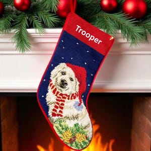 May include: A navy blue Christmas stocking featuring a white dog wearing a red Santa hat and a red and white striped scarf. The top cuff is red with the name Trooper embroidered in white. The stocking has a red trim and a hanging loop.