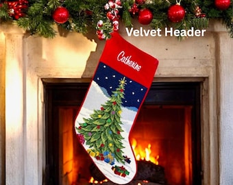 May include: A red and white Christmas stocking with a personalized name, "Catherine," embroidered on the red velvet header. The stocking features a detailed needlepoint design of a Christmas tree, snow, and presents. The stocking hangs in front of a fireplace.