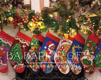 Puede incluir: Ocho calcetines de Navidad rojos y azules con diseños bordados de un cascanueces, un árbol de Navidad, un tren de juguete, un oso de peluche, un caballo de balancín y un muñeco de nieve. Los calcetines están colgados en una repisa de chimenea decorada con vegetación y luces. El texto "BA BARKER GIFTS STOCKINGS & ACCESSORIES" es visible en la parte inferior de la imagen.