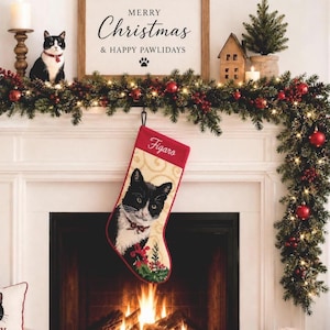 May include: A Christmas stocking featuring a woven image of a black and white tuxedo cat with the name Figaro embroidered in white script at the top. The stocking has a cream background with a subtle swirl pattern and a festive holly design.