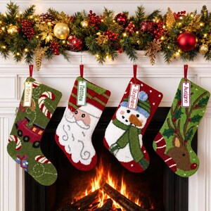 May include: Four personalized Christmas stockings hanging in a row. The first is green with a train and candy canes, the second features Santa Claus, the third a snowman, and the fourth a reindeer. Each stocking has a white name tag attached.