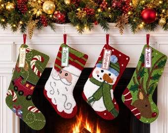 May include: Four personalized Christmas stockings hanging in a row. The first is green with a train and candy canes, the second features Santa Claus, the third a snowman, and the fourth a reindeer. Each stocking has a white name tag attached.