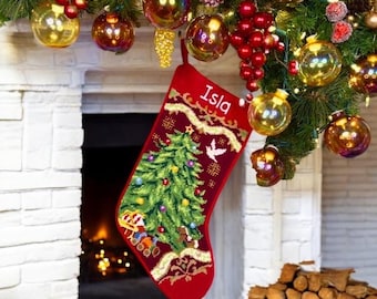 May include: A red Christmas stocking featuring a needlepoint design of a green Christmas tree with colorful ornaments, a small train at the base, and a white dove. The name Isla is embroidered in white at the top, bordered by gold trim.