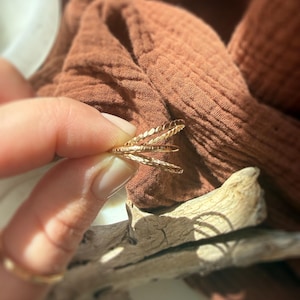 May include: A set of three thin gold rings featuring distinct textures, including a twisted rope design, a smooth band, and a hammered finish, stacked together to create a layered appearance with a metallic luster and reflective surface.