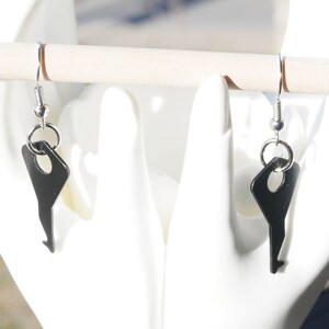 May include: A pair of silver key-shaped earrings with black key charms hanging from the hooks.