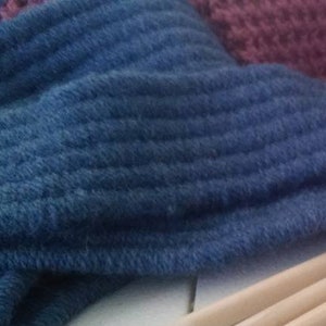 Könnte beinhalten: Nahaufnahme einer blauen Stricksocke mit drei Holzstricknadeln. Die Nadeln liegen auf einer weißen Oberfläche.