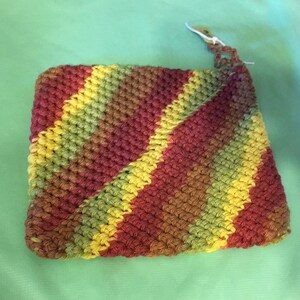 Peut inclure: Un dessous de plat crocheté avec un motif rayé diagonal en nuances de rouge, jaune et vert.