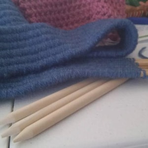Könnte beinhalten: Drei Stricknadeln aus Holz mit einem blauen Strickstoff drumherum.