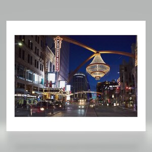 May include: A large, illuminated chandelier hangs over a city street at night. The street is lined with buildings, including the Playhouse Square theatre. The scene is lit by streetlights and the glow of the chandelier.
