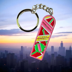 May include: A pink, red, yellow, and green hoverboard keychain with a silver chain and key ring. The keychain has the words "HOVER BOARD" in yellow. The background is a cityscape with a sunset.