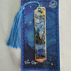 May include: A metal bookmark featuring Van Gogh's "Starry Night" painting, with a blue tassel. The bookmark is gold-colored with a detailed cutout design. The bookmark is on a blue card with the words "Van Gogh".