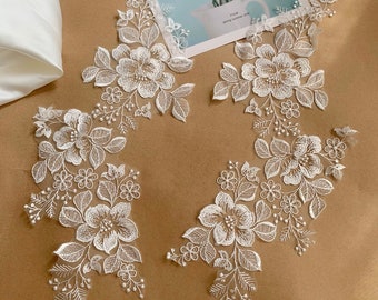 Puede incluir: Dos piezas de encaje floral blanco con bordado delicado. El encaje está sobre un fondo marrón.