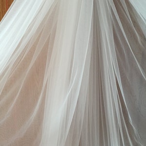 May include: White tulle fabric with a soft, flowing texture. The fabric is draped and folded, creating a delicate and airy appearance.