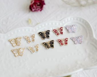 May include: A collection of small butterfly-shaped appliques featuring intricate embroidery and metallic thread details. The set includes various colors such as gold, black, red, and silver, arranged on a white scalloped decorative tray.