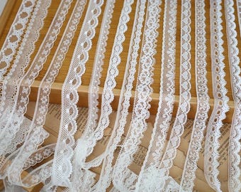 May include: A collection of eleven distinct white lace trim strips arranged vertically. Each strip features a unique woven pattern, including floral motifs, scalloped edges, geometric shapes, and intricate openwork designs, all displayed in a parallel layout.