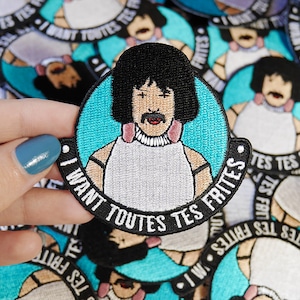 Op de afbeelding: Een blauwe en witte geborduurde patch met een cartoon van Freddie Mercury met de tekst "I want toutes tes frites" in zwart.