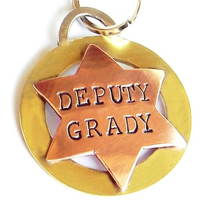 May include: A gold and copper sheriff's star shaped dog tag with the text "DEPUTY GRADY" engraved on it.