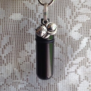 May include: A black metal keychain with a small silver charm of a cat holding a ball. The keychain has a loop for attaching to a bag or belt.
