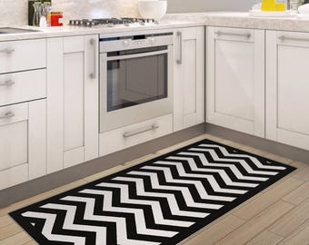 May include: Black and white chevron patterned kitchen rug in a modern kitchen with white cabinets and stainless steel appliances.