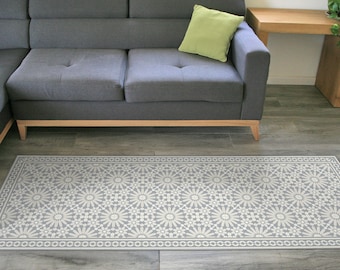 Puede incluir: Una alfombra gris y blanca con un diseño geométrico. La alfombra se coloca delante de un sofá de esquina gris con un cojín verde.