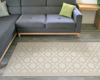 Puede incluir: Una alfombra de área beige y blanca con un diseño geométrico. La alfombra se coloca frente a un sofá seccional gris con una almohada de tiro verde.
