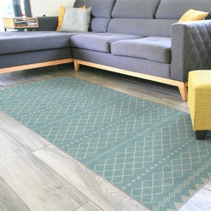 May include: A light blue area rug with a geometric pattern in a lighter shade of blue. The rug is laid out on a wood floor in front of a gray sectional sofa.