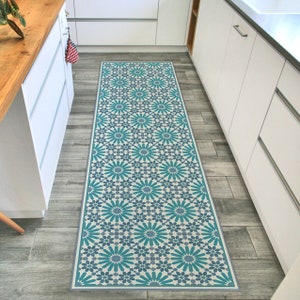 May include: A teal and white patterned kitchen runner rug with a geometric design. The rug is placed on a wood floor in a kitchen.