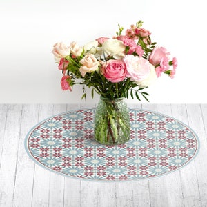 May include: A round, blue and white patterned table mat with a red floral design. A clear glass vase with pink and white flowers sits on the table mat.