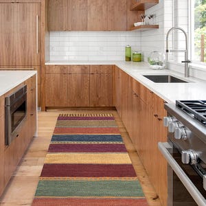 May include: A kitchen with wood cabinets and a white countertop. A striped rug is on the floor in front of the cabinets. A stainless steel stove is on the right side of the image.
