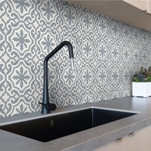 May include: A kitchen scene featuring a black sink and faucet against a backdrop of patterned tiles. The tiles display a repeating gray and off-white floral design. A white planter with succulents sits on the countertop.