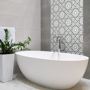 May include: A white freestanding bathtub in a modern bathroom with gray tiled walls. The wall behind the tub features a decorative tile pattern with white flowers on a gray background.