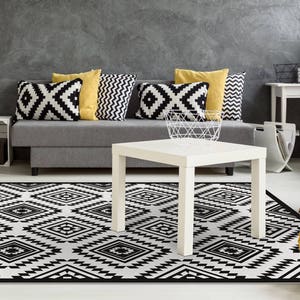 May include: A black and white geometric patterned rug with a gray sofa and a white coffee table in the background. The sofa has black and white patterned pillows and yellow pillows.