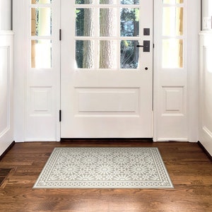 May include: A white doormat with a grey and white geometric pattern. The doormat is placed in front of a white door with a glass pane.