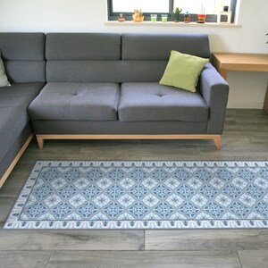May include: A blue and white patterned rug with a geometric design. The rug is placed in front of a gray sectional sofa with a green pillow.