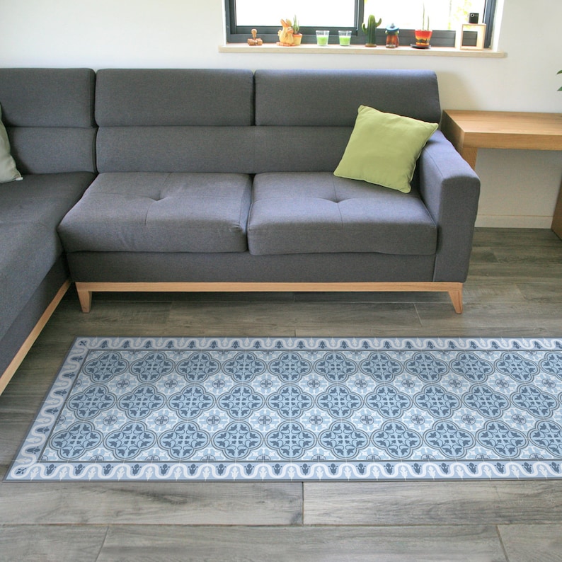 May include: A blue and white patterned rug with a geometric design. The rug is placed in front of a gray sectional sofa with a green pillow.
