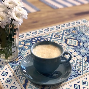 May include: A blue and white patterned placemat with a blue cup of coffee on top. The placemat has a geometric design with squares and diamonds.