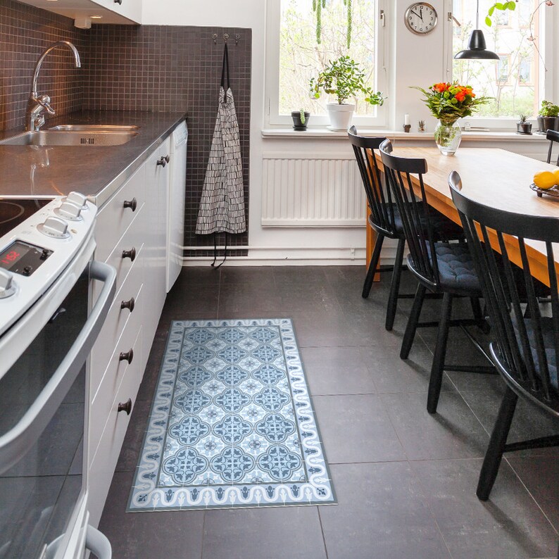 May include: A blue and white patterned kitchen rug with a geometric design. The rug is placed in a kitchen with white cabinets and a black and white tiled backsplash.